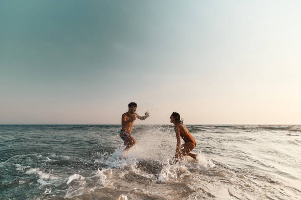 cheerful couple having fun while splashing each other at sea. - travel stock pictures, royalty-free photos & images