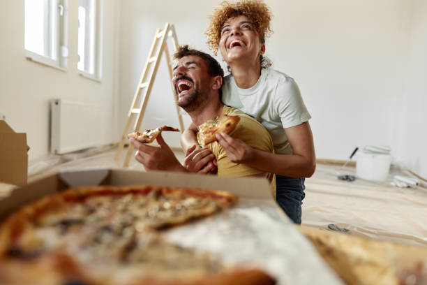 cheerful couple in love eating pizza on a break from home renovation process. - junk food stock pictures, royalty-free photos & images