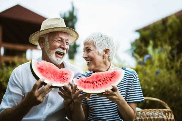 cheerful mature couple having fun while eating watermelon during picnic day in nature. - food stock pictures, royalty-free photos & images