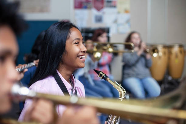 cheerful mixed ethnicity asian girl with saxophone in band orchestra class - concert stock pictures, royalty-free photos & images