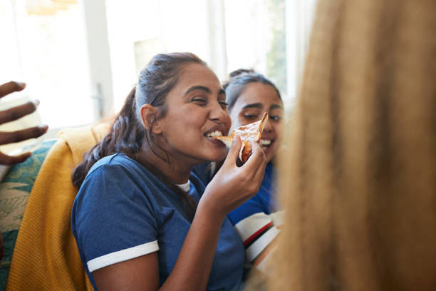 cheerful young woman eating slice of pizza - junk food stock pictures, royalty-free photos & images