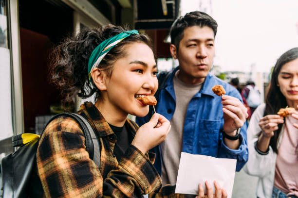 cheerful young woman eating street food with friends - food stock pictures, royalty-free photos & images