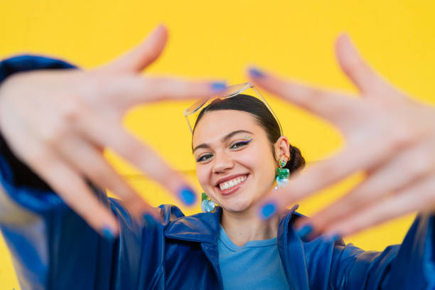 cheerful young woman smiling, framing face with hands against bright yellow backdrop - fashion stock pictures, royalty-free photos & images