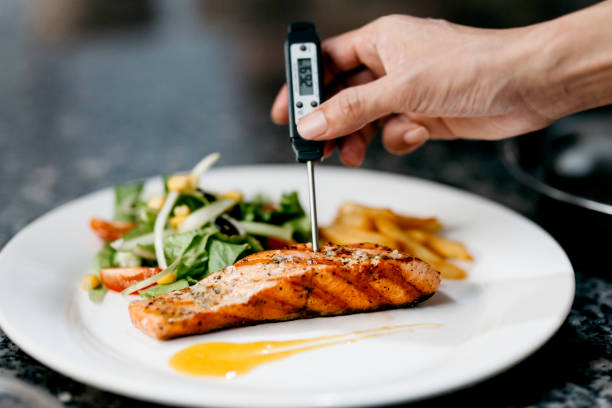 chef utilise un thermomètre pour mesurer la température du filet de saumon poêlé - food photos et images de collection