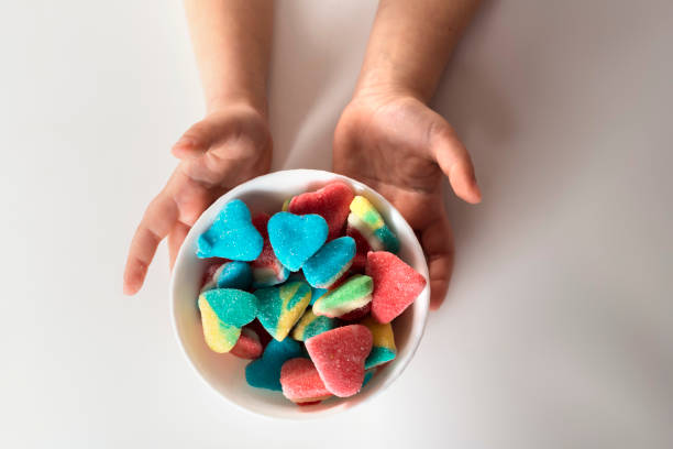 child hands holds a bowl with colorful sour and sweet candies on a white background. - junk food stock pictures, royalty-free photos & images