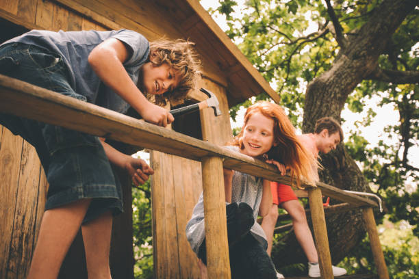 childhood friends hammering and working to build their treehouse - home decoration stock pictures, royalty-free photos & images