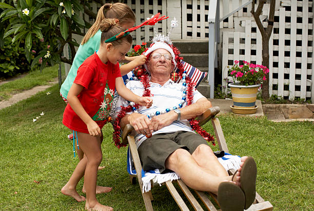 children (7-9) decorating senior man with christmas decorations in yard - garden decoration stock pictures, royalty-free photos & images