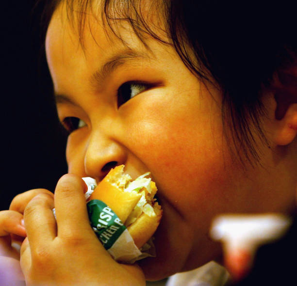Chinese girl eats a hamburger at an American fast food chain for an activity to mark International Children's Day with her parents on May 31, 2005 in...