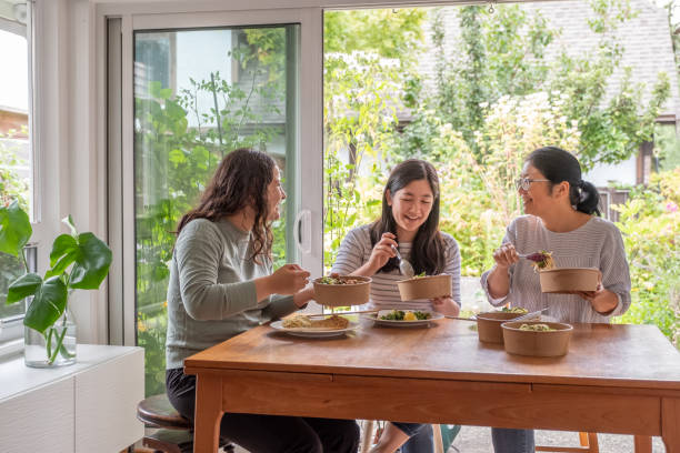 chinese mother, eurasian daughters eating vegan takeout in re-useable containers - junk food stock pictures, royalty-free photos & images