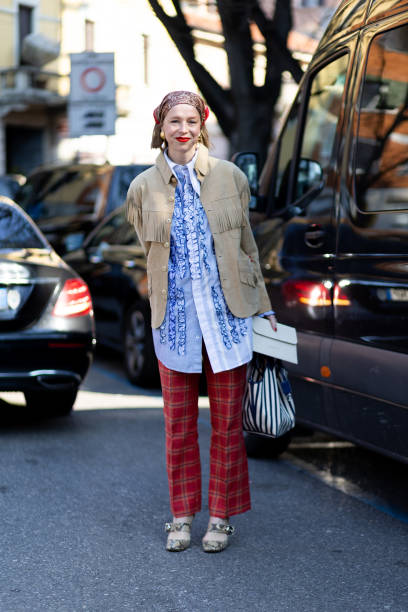 Chloe King wears a red printed bandana, gold pendant earrings, a blue shirt with ruffles, a beige suede jacket with fringes, red checked flared...