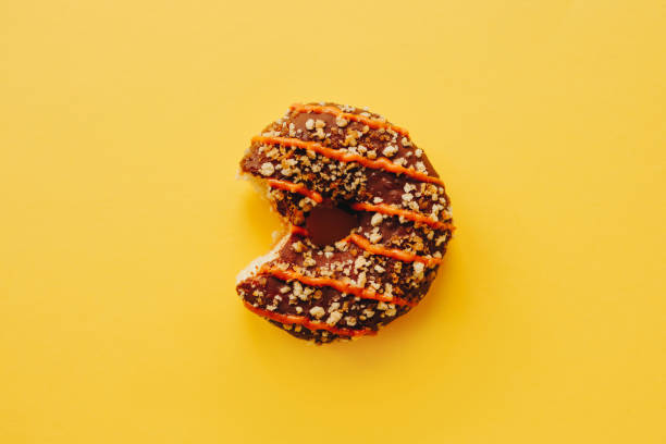chocolate doughnut with bite on yellow background - junk food stock pictures, royalty-free photos & images