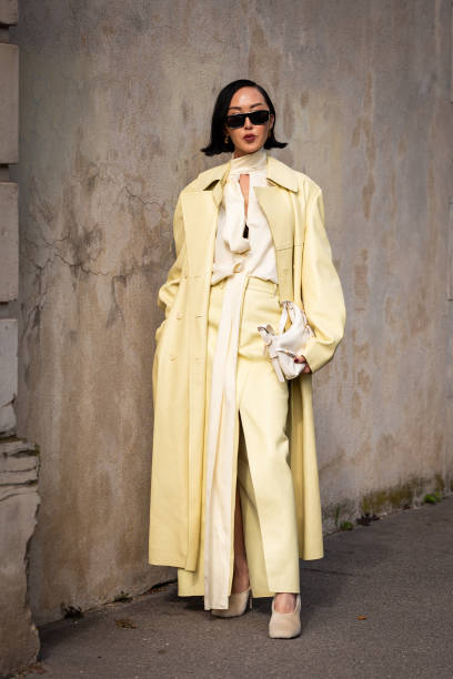 Chriselle Lim wears a light yellow blouse, yellow trousers, yellow leather long coat, beige heels and white Givenchy bag, outside Givenchy, during...