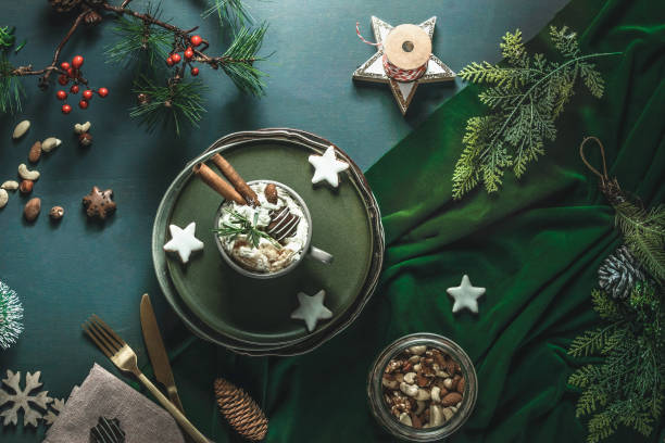 christmas background with hot chocolate with cream, biscuits, cutlery, nuts and fir green at green table - food stock pictures, royalty-free photos & images