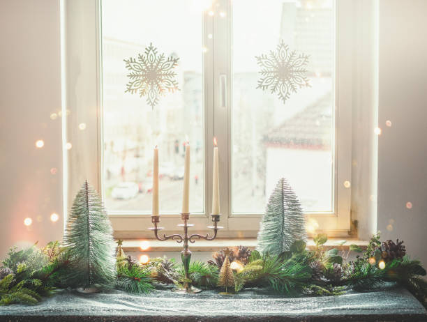 christmas home decoration with candlestick, christmas trees, fir green and pine cones on table with table cloth at window background with hanging snowflakes - home decoration stock pictures, royalty-free photos & images