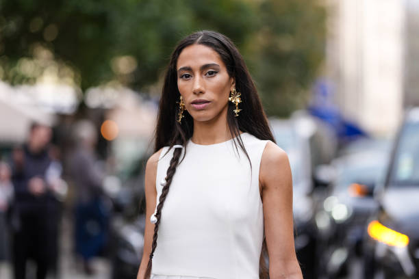 Ciinderella Balthazar wears braided hair with pearl detail, gold earrings, white sleeveless pleaded sheer mesh Akris maxi dress, outside Akris,...