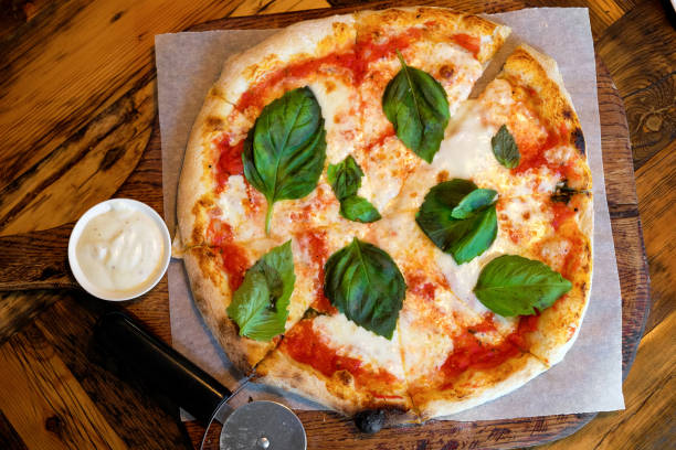 circle pizza margarita with mozzarella and basil leaves on a wooden stand or cutting board, on the table in a cafe or fast food restaurant. traditional italian cuisine. vegetarian food. - junk food stock pictures, royalty-fre