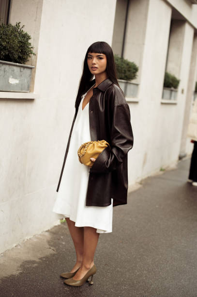 Clara Kong Vila wears white dress, brown high heels, black leather jacket and yellow bag outside the LOEWE presentation during the Womenswear...