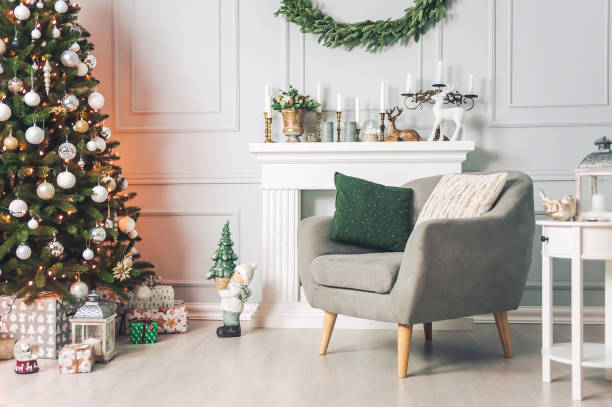 classic interior with an armchair tables, and a christmas tree with decorations on a light background of a wall with a fireplace. - home decoration stock pictures, royalty-free photos & images