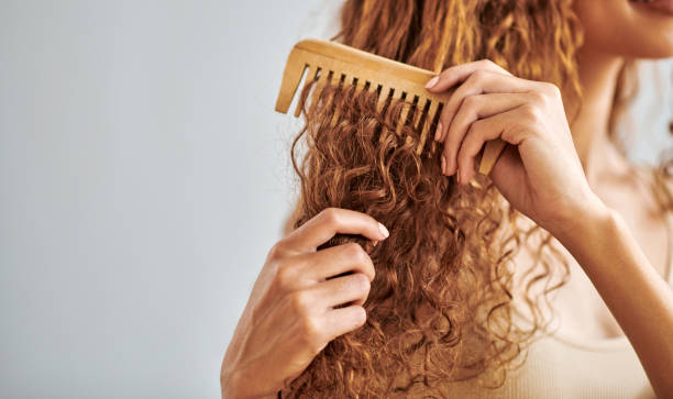 cleaning, beauty and hair care by woman brush and style her natural, curly hair in bathroom in her home. hygiene, frizz and damage control with female hands comb natural hair in morning routine - hairstyle stockfoto's en -bee