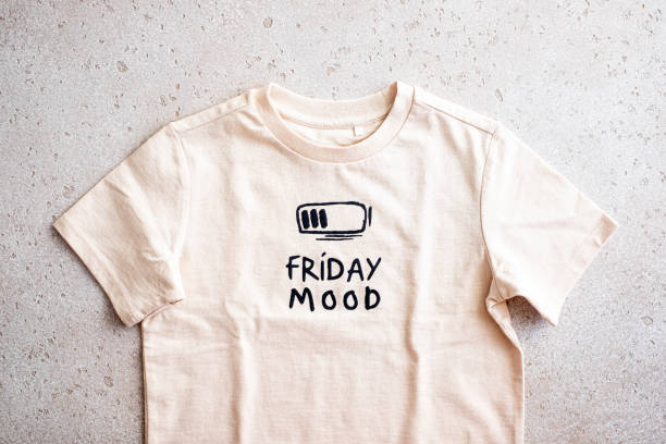 close-up of beige t-shirt with a print “friday mood” on light background, top view - fashion stock pictures, royalty-free photos & images