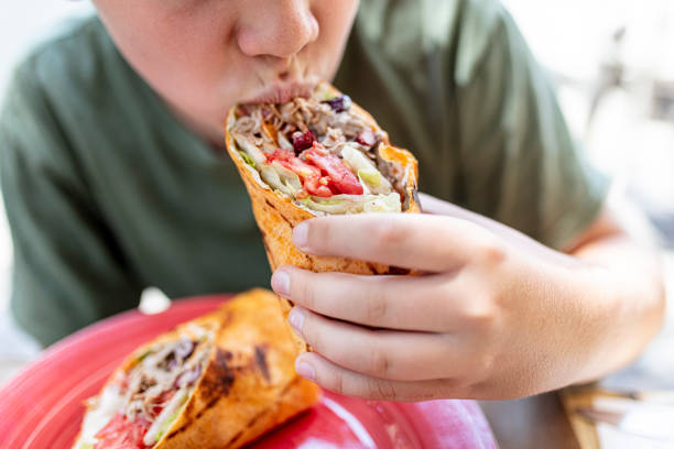close-up of boy holding and eating wrap sandwich - junk food stock pictures, royalty-free photos & images