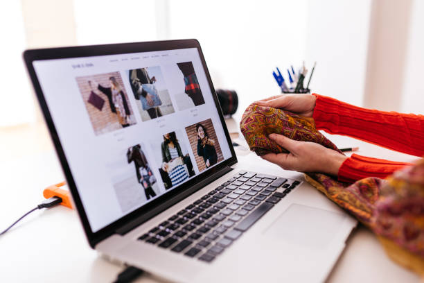 close-up of fashion designer in studio with laptop examining fabric - fashion stock pictures, royalty-free photos & images