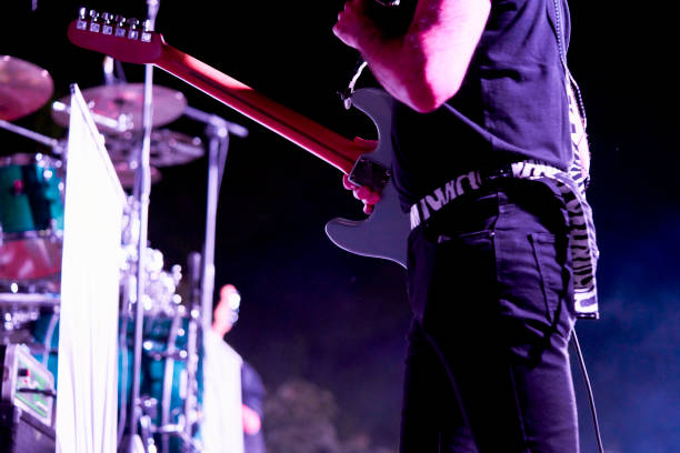 close-up of rear view of midsection of a performer standing playing his guitar in front of the blurry audience in a concert - concert stock pictures, royalty-free photos & images
