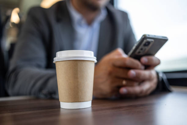 close-up of takeaway coffee on desk with businessman using smartphone - junk food stock pictures, royalty-free photos & images