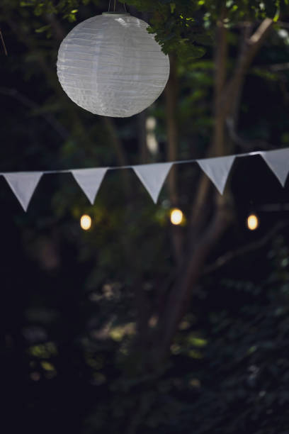 close-up of white flag garland and paper lantern against trees. garden party, summer festival, birthday party, baptism or wedding. - garden decoration stockfoto's en -beelden