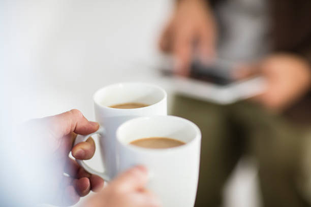 close-up of woman holding coffee cups while man using tablet in office - coffee stockfoto's en -beelden