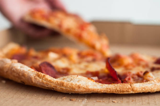 close-up view of pizza with one person's hand taking a slice - junk food stock pictures, royalty-free photos & images