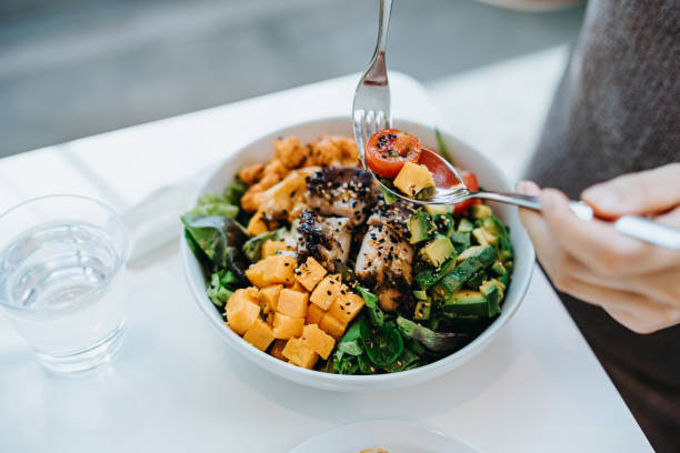close up, high angle shot of young woman enjoying multi-coloured healthy fruit, vegetables with grilled chicken salad bowl with balanced nutrition in cafe, with a glass of water by the side. healthy eating lifestyle. people,
