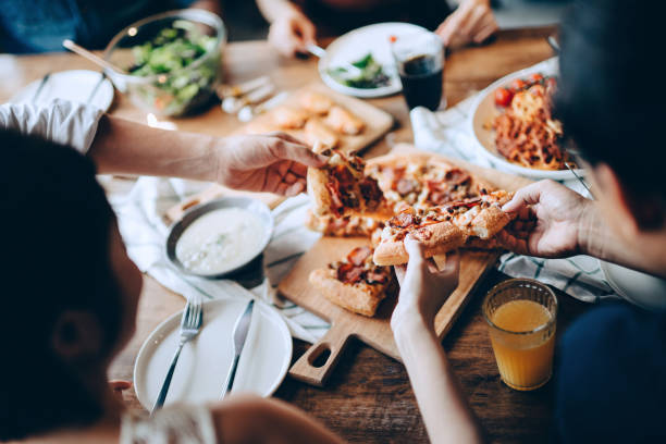 close up of a young group of friends passing and serving food while enjoying together. they are having fun, chatting and feasting on food and drinks at dinner party - food stock pictures, royalty-free photos & images