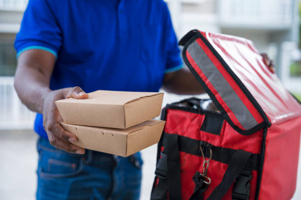 close up of an unrecognizable courier man making food delivery, carrying takeaway paper boxes to your doorstep. - junk food stock pictures, royalty-free photos & images