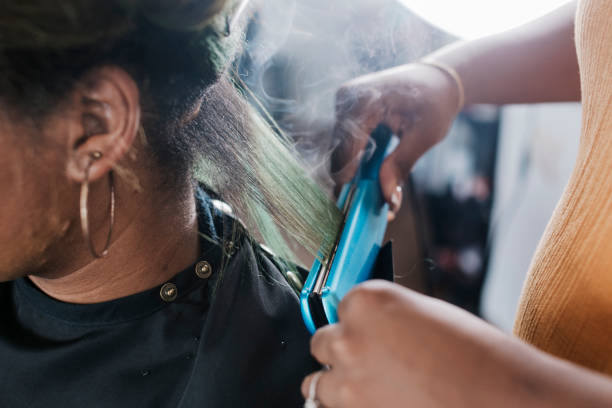 close up of black hairdresser straightening client's hair - hairstyle stock pictures, royalty-free photos & images