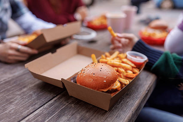 close up of burger in box on a table with teenagers around it - junk food stock pictures, royalty-free photos & images