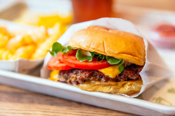 close up of juicy cheeseburger with fresh tomatoes - junk food stock pictures, royalty-free photos & images