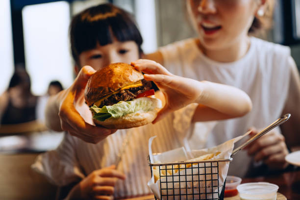 close up of lovely little asian girl and her mother dining out in restaurant, sharing burger and french fries together. asian family enjoying a happy meal. family eating out lifestyle - junk food stock pictures, royalty-free