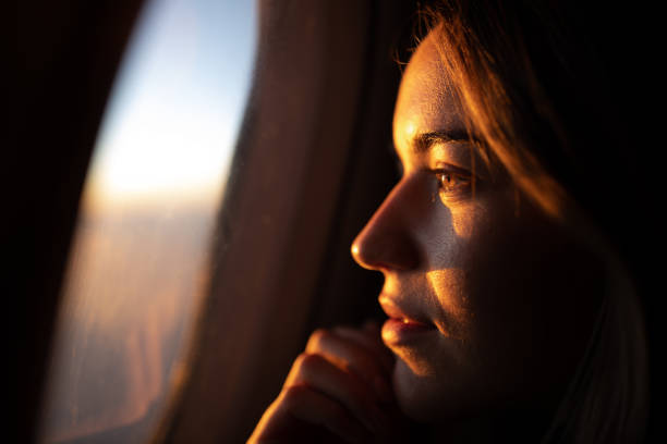 close up of pensive woman looking at sunset through airplane window. - travel stock pictures, royalty-free photos & images