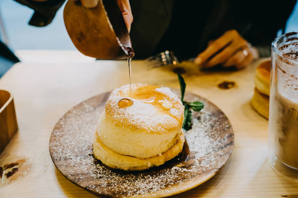 close up of woman drown the souffle pancake in maple syrup - junk food stockfoto's en -beelden