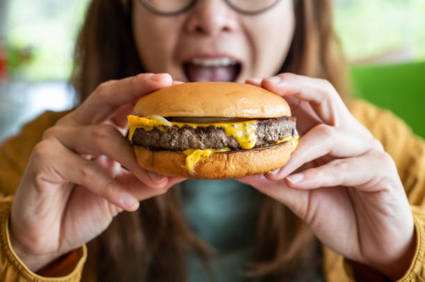 close up of woman opened her mouth to eat a classic beef cheeseburger. - junk food stock pictures, royalty-free photos & images