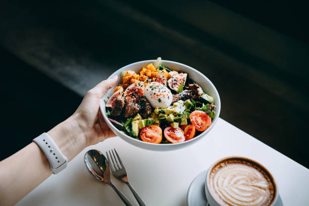 close up of woman's hand holding a bowl of fresh beef cobb salad, serving on the dining table. ready to enjoy her healthy and nutritious lunch with coffee. maintaining a healthy and well-balanced diet. healthy eating lifestyl