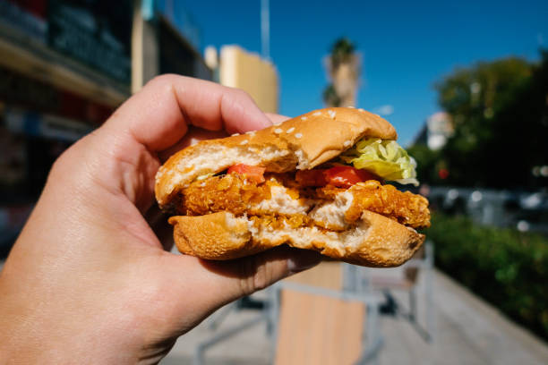 close up view of man holding chicken burger, in background blurred image of city. - junk food stock pictures, royalty-free photos & images