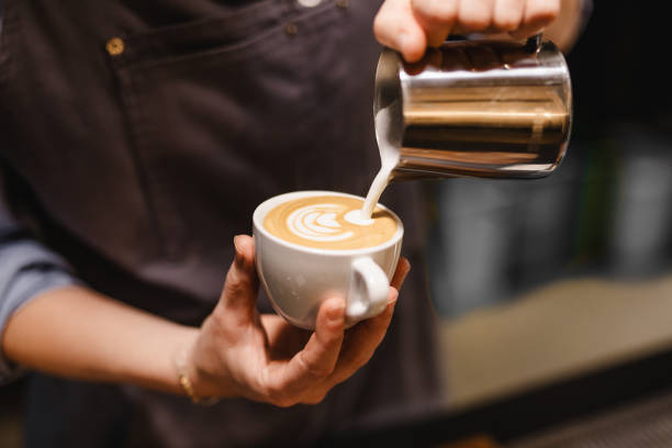 close up view of young woman preparing a coffee by drawing a flower with milk - coffee stock pictures, royalty-free photos & images
