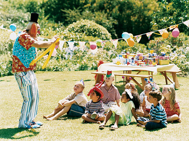 clown entertaining children sitting on the grass at a birthday party - garden decoration stock pictures, royalty-free photos & images