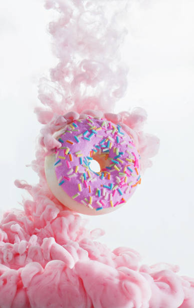 colorful pink cloud around a sweet donut with sprinkles. dissolving paint on a white background with copy space - junk food stock pictures, royalty-free photos & images