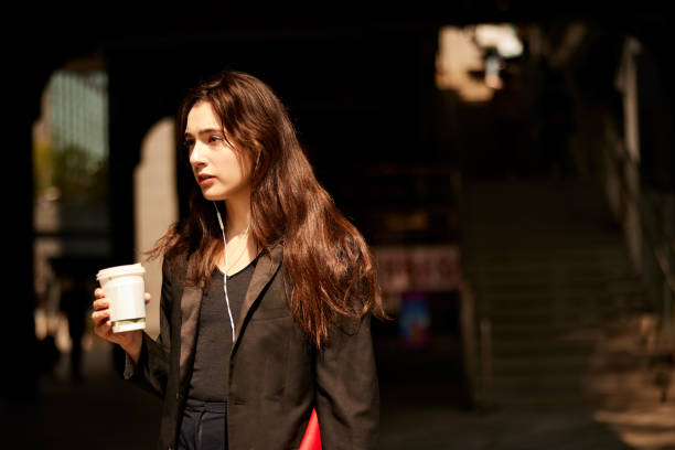 commute harmony: businesswoman in suit listens to music with coffee in hand. - junk food stock pictures, royalty-free photos & images