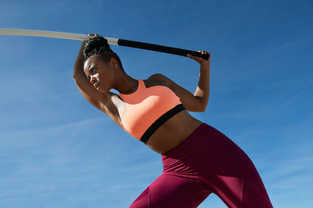 confident sportswoman holding pole vault against blue sky - fashion stock pictures, royalty-free photos & images