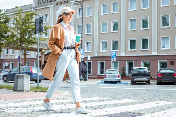 confident young lady strolls along paved sidewalk in downtown taking sips from coffee cup - fashion stock pictures, royalty-free photos & images