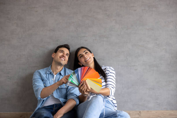 couple at home thinking about painting the walls and holding a color swatch - home decoration stock pictures, royalty-free photos & images